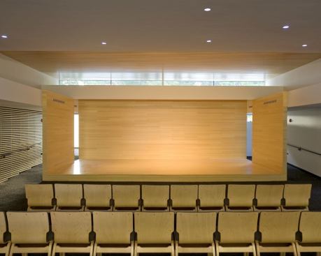 Daylight in combination with electric light frames the sanctuary stage. Flush-mounted MR16 downlights configured in an irregular pattern provide general lighting for the seating area.
