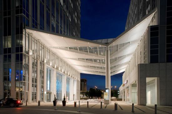 The canopy consists of folded solid metal and fritted glass panels, uplit with 150W T6 3000K metal halide fixtures located along the sides. Based on a detailed reflection study, the lighting designers determined that point sources would minimize the visibility of the fixtures reflected on the glass ceiling panels.