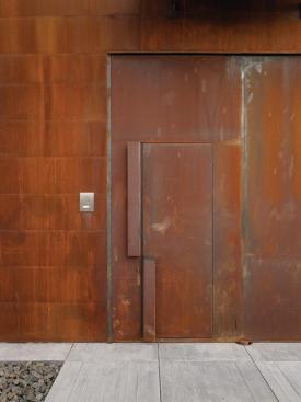 The entry door blends with the surrounding wall, with only its folded steel handles indicating its function.