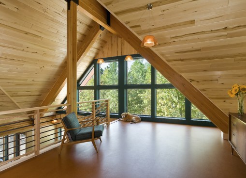 Interior of A-frame cabin with wood paneling and large windows as seen from loft space
