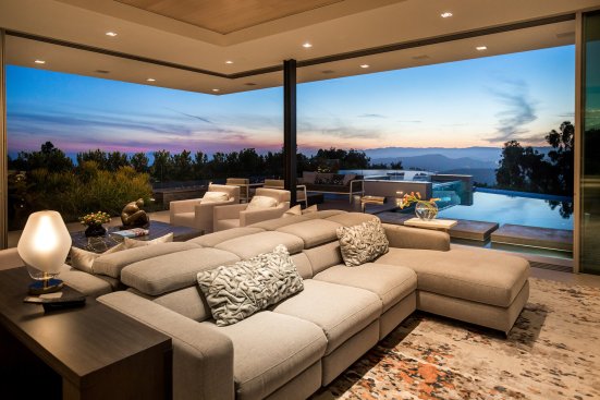 Luxury modern home living room with open glass walls and views of the pool and sunset sky.