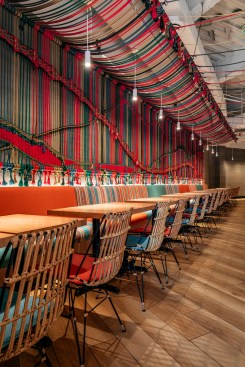 Orange and teal banquets line the wall adorned with a multi-color handwoven macramé rope mural made of 137 pieces measuring 34 feet long created by a local artist. 
