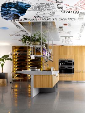 Lignum plays on contrasting material—stone and wood or stainless steel and wood—to create a sculpturelike island that incorporates a ceiling-mounted range hood and visually connects with the nearby tall wall cabinetry and wine conservation units.