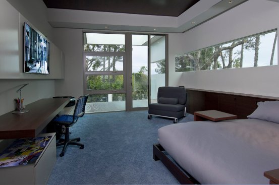 Modern home bedroom with desk workspace, TV and floor to ceiling windows.