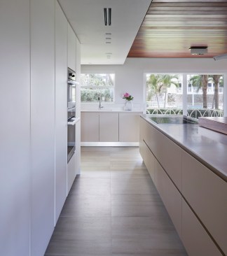 The large matte taupe kitchen island is topped with a thick, cantilevered live-edge Ipe wood slab, and oriented parallel to the cabinetry in an effort to maintain the flow and circulation of the space.