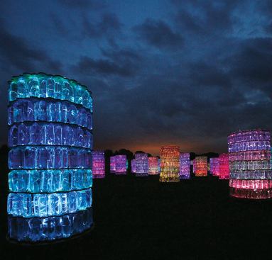 Water Towers is located in the area of Longwood known as the Meadow at Hourglass Lake. According to Munro, this piece "marks the transition between Longwood’s formal gardens and its natural landscape." The light installation is composed of 69 structures, each built out of water-filled 1-liter recyclable plastic bottles stacked on plywood boards for intermediary support. Fiber-optic strands are threaded through all 17,388 bottles and connected to an LED projector with a hand-painted color wheel. During the day, the combination of plastic and water has the appearance of glass, and the towers take on different levels of transparency in the natural light. At night, in the darkness of the summer sky, the towers take on a completely different personality and resemble vertical haystacks of colored light. The experience is further enhanced with a sound track of choral music.