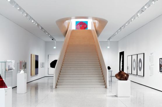 The new entry stair, with its sculptural form, is as much a piece of artwork as the other objects on display. LED spotlights in a semi-recessed ceiling slot illuminate the mixed media on display.