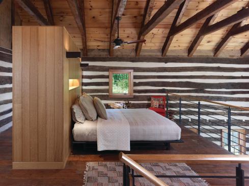 In the master bedroom, a modern built-in headboard and steel railings contrast with historic log walls.