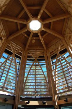 Here, arched wooden trusses overhead suggest a canopy of tree branches that filters the sunlight by day. Simulating the sun at the top, fluorescent fixtures located behind a circular diffuser give an ambient glow day and night. Located on the horizontal beams, mono-points with 35W, 3000K, PAR30 metal halide lamps graze up the wood trellis around the room.