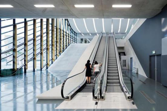 On+the+ground+floor%2c+visitors+enter+under+the+cantilevered+form+of+the+m%c3%a9diatheque+and+use+escalators+to+access+the+upper+levels.+Floor+detailing+echoes+the+lines+of+the+louvers+and+the+lights+above.