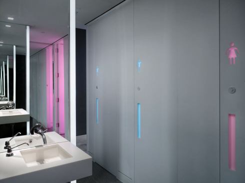 The communal restroom has private stalls and the gender designation for each is reinforced with color. A resin panel, inserted in the door, allows the gender symbol and handle to glow with color.