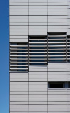 The façade features a faceted surface of terracotta modules, traversed by a dynamic sequence of multi-height openings.