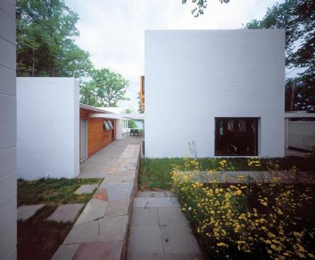 Salmela pointed the cabin toward the lake and used glazed side walls to broaden water views. Masonry walls bracket the cypress clad cabin, sauna, and garage. The outdoor rooms are framed with white stained wood and screened with 2x2 slats.