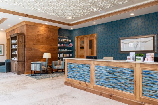 The waiting rooms, called Living Rooms, feature upholstery patterns and rustic wood floors that reference the Floridian Cowboy theme, with wood-accented but distinctly contemporary chandeliers set against a more traditional coffered ceiling made of Ceilume thermoformed panels.