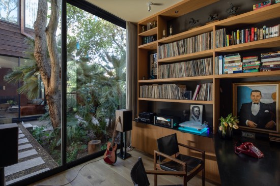 The home office offers direct access to the atrium garden, connecting to the library/media room beyond. Custom, built-in rift oak and blackened steel casework showcases the husband's extensive vinyl music collection, high performance audio equipment, and a variety of personal affects, objects, and art.