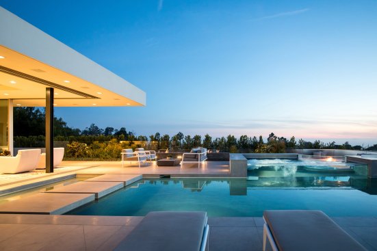 Indoor outdoor living room connects to pool terrace with sliding glass walls at modern Beverly Hills home.