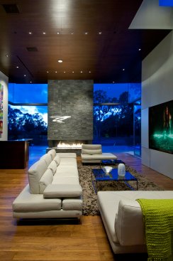 Luxury modern living room design with double height glass walls and stacked stone fireplace.
