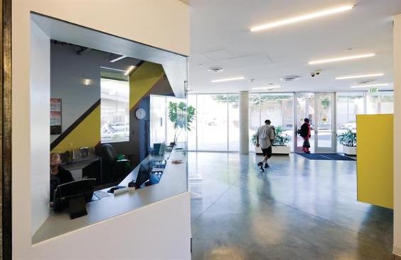 The entry lobby sets the stage for the materials palette used throughout the building: concrete floors, white walls with yellow accents, and ceiling-mounted linear light fixtures.
