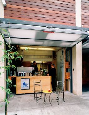 Ground-level garage doors lift up, creating inviting sidewalk space for the Blue Bottle Coffee kiosk.
