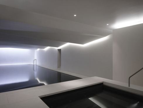 Turning past the sauna, the pool, internally clad with black Sicilian Basaltina, comes into view. The play of light cast across the undulating GRG ceiling above is mirrored in the water below. A skylight at the far end of the pool and tucked-up out of view, illuminates the end wall naturally by day. At night, this is balanced with electric light to reflect light across the space, modeling and accentuating the ceiling's sculptural form.