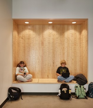 Students find a moment of respite during a busy school day in an inset bench surrounded by warm wood tones and calming lighting. The space utilizes Trauma Informed Design principles. 