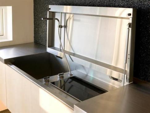 The stainless steel countertop along the rooms textured stone wall lifts to reveal a recessed sink and cooktop. 