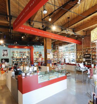 Sixth Floor Museum Store + Café- Dallas, TX The SFM Store + Cafe is a small adaptive use project overlooking Dealey Plaza. The project provides an immersive retail environment for the museum's gift shop, including a 34-seat casual café. The design aims to work with the existing building--a turn of the century warehouse building-- in a'ship-in-a-bottle' strategy that touches the shell lightly with a clean lined and modern design that clearly differentiates new from existing. A new exterior sign carefully woven in the historic façade hints at the new interior. The angles present in the arrangement of program elements respond to the desire lines and views to the components of the museum's campus: the site of the event and the entry to the museum. Scarlet fragments of these visual frames appear as a motif that ties the diverse functions into a cohesive whole. The colorful design elements effectively establish a fresh look for the museum's branded image.
Architect: Corgan Associates
