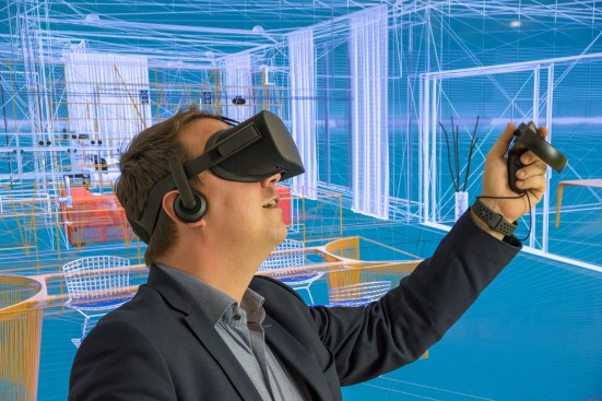 Virtual reality and mixed reality at the Autodesk VR Center of Excellence in Munich, Germany. Mixed reality showing a man with VR goggles immersed in a virtual architectural 3d wireframe environment.