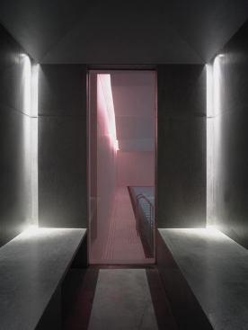 Dark interior finishes and moody lighting characterize the sauna and steam room. Illumination is provided by corner recessed vertical slots and partially concealed louvered downlights.