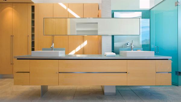 Wide drawers with recessed aluminum handles hold quotidian bathroom supplies, glass shelves behind a stainless steel shower screen house shampoo and soap.