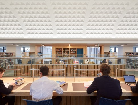 Custom desk tasklighting provides illumination for the reading tables that flank the library's central double-height area.