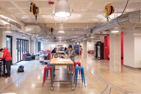 The first-floor research and development space contains a fabrication shop and robotics lab. A red double-height huddle space (at right) punches through to the research level above (seen on the opening spread).