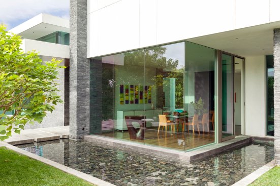 Glass wall dining room with outdoor pond view at modern Beverly Hills home.