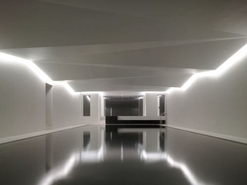 The pool's ceiling is halo-lit from its angular perimeter with two concealed indirect sources, which bounce light down the walls and define the structure's peaks and troughs with a distinct line of light. Crisp white 3500K cold cathode sources illuminate the space by day.