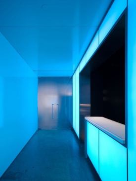 The entry coat check area was fashioned as a portal. The polished surfaces reflect light for a dramatic entrance. The glass walls are backlit with a series of RGB LED modules. Due to the restricted wall depth of 3 inches, the LED modules are mounted tightly together and can display patterns and low-resolution animation. Concealed track fixtures accent the desk.