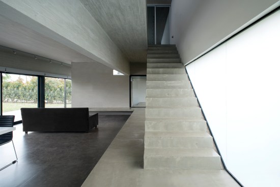 The exposed concrete stair anchors the southern edge of the open-plan first-floor living space.