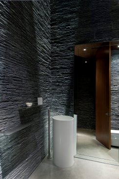Modern design powder room bathroom with textured stacked slate walls and minimalist pedestal sink at Beverly Hills home.