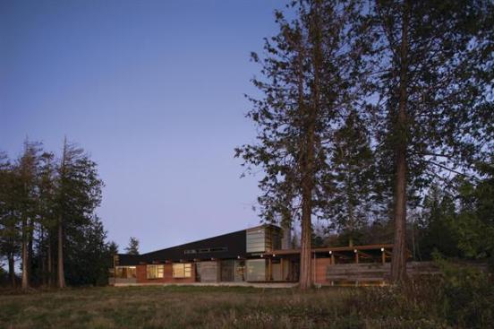The roof over the living room slopes up to welcome natural daylight. The higher volume is clad in black-stained cedar. A lower volume wrapped in reclaimed barnwood and weathering steel houses the kitchen and sunroom.