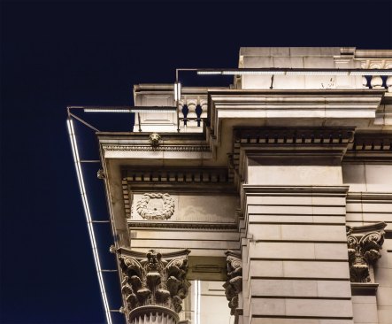 A custom mounting bracket system supports the custom-designed grazing luminaires, which feature two fixture heads, one with a 9-degree beam spread to illuminate the upper cornice and one with a 34-degree beam spread to wash the lower portion of the façade.