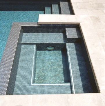 Jimmy Reed custom built this gorgeous spa and used his signature strip of real white gold glass tiles to accent the shape and form of the custom benches, treads and stairs.
