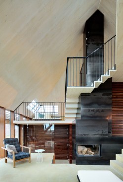 Terraced platforms lined with walnut cabinetry form a continuous set of living spaces that spiral around the house’s central chimney.