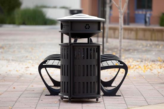Urban Renaissance Litter & Recycling Receptacle shown in side opening with integrated recycle bin configuration with Vertical grillwork; also shown Trio Benches in 6 foot, backed configuration with Black Texture powdercoated frame, extruded aluminum slats and two armrests at BART, Pleasant Hill/Contra Costa Centre Station, Walnut Creek, California