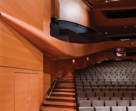 The warmth of the moabi veneer-and-resin panels is the hall's defining feature; they clad everything from the walls and balcony to the tip-and-fly panels on the ceiling and pivoting stage panels. The latter can be easily moved to change the acoustics for different types of musical performances, as well as film, theater, and dance events.