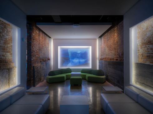 Entering the lounge, Salon D is directly in front of you. The gypsum frames float from the wall on a pillow of white light. Linear LED fixtures provide this effect and the fixture's slim profile kept the gypsum elements slim as well. In the center, an array of light, frames a video art projection. The LED sources allowed this effect to continue throughout the lounge and still meet the governing energy codes.
