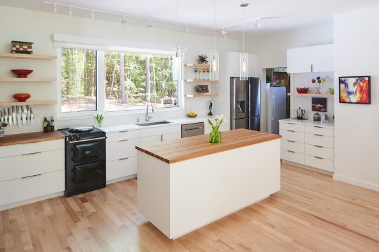 The all-white kitchen features an Aga stove, work island, floating shelves, and a coffee station.