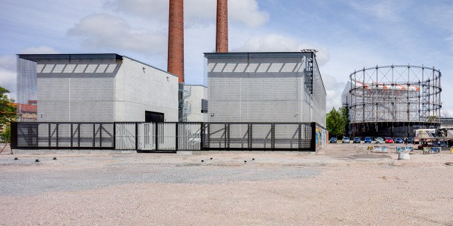 The substation sits directly next to the decommissioned 1909 Suvilahti power plant (whose brick stacks can be seen beyond), which has since been turned into a cultural center.