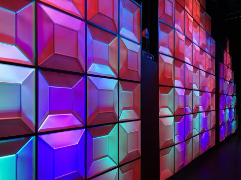 Backlit, the faceted panels have a gem-like appearance, and the wall becomes a glowing array of different-colored planes. 