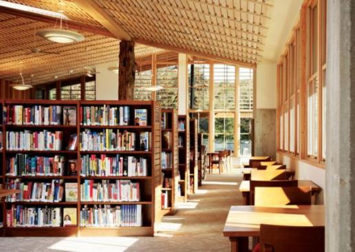 The reading room that holds the main collection of the Portola Valley Library is an airy and light-filled space thanks to floor-to-ceiling windows and skylights. The wall paneling and ceiling slats?elements that appear in all three main buildings?are made from milled Douglas fir roof decking salvaged from the dismantled school.