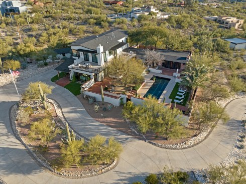 Elevating a 1949 home to new heights, this addition and remodel seamlessly merges history and contemporary allure. The expansion from 2485 to 7560 square feet crafts an exquisite space. Striking black-framed doors and windows contrast with red adobe charm. A balcony beckons, overlooking a desert oasis with a pool, palms, and a regal saguaro.