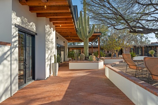 A solitary saguaro commands attention within its retaining wall enclosure, surrounded by a welcoming red brick patio. The nearby double doors offer a seamless passage into the inviting great room. Amongst the carefully landscaped surroundings, mesquite trees cast serene shadows, crafting inviting pockets of shade.